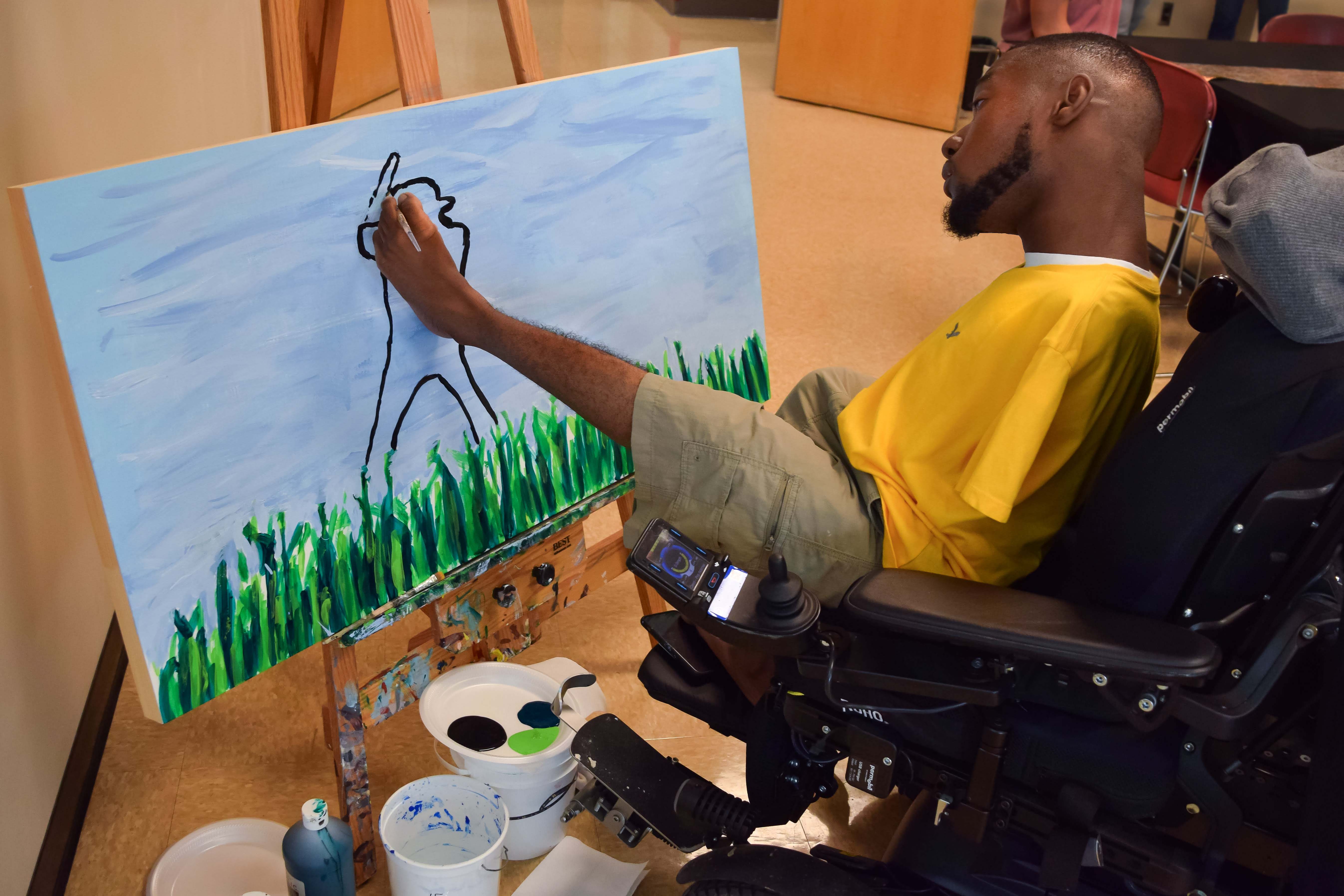 Student in wheelchair paints with his feet