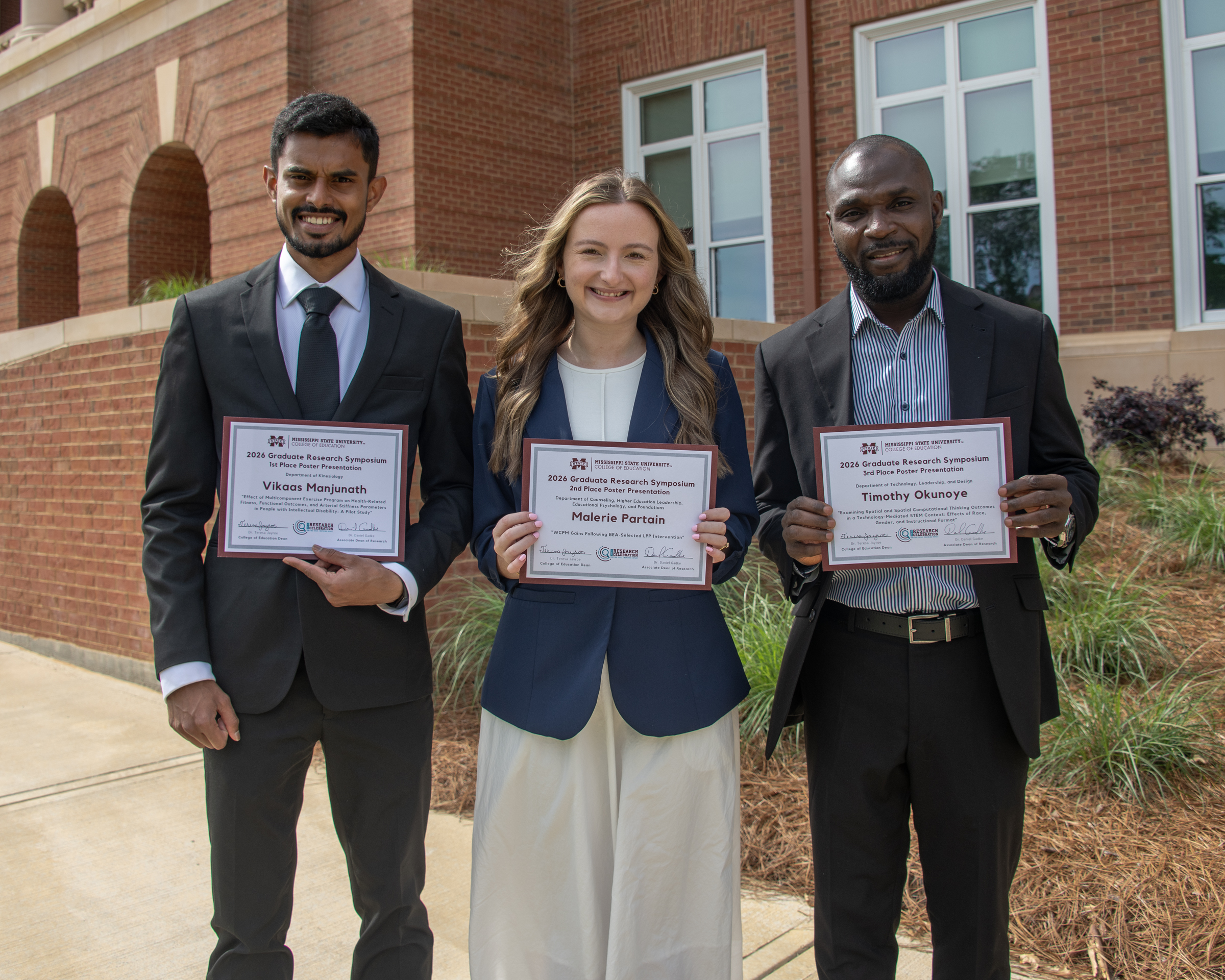 Photo of three students holding certificates outside
