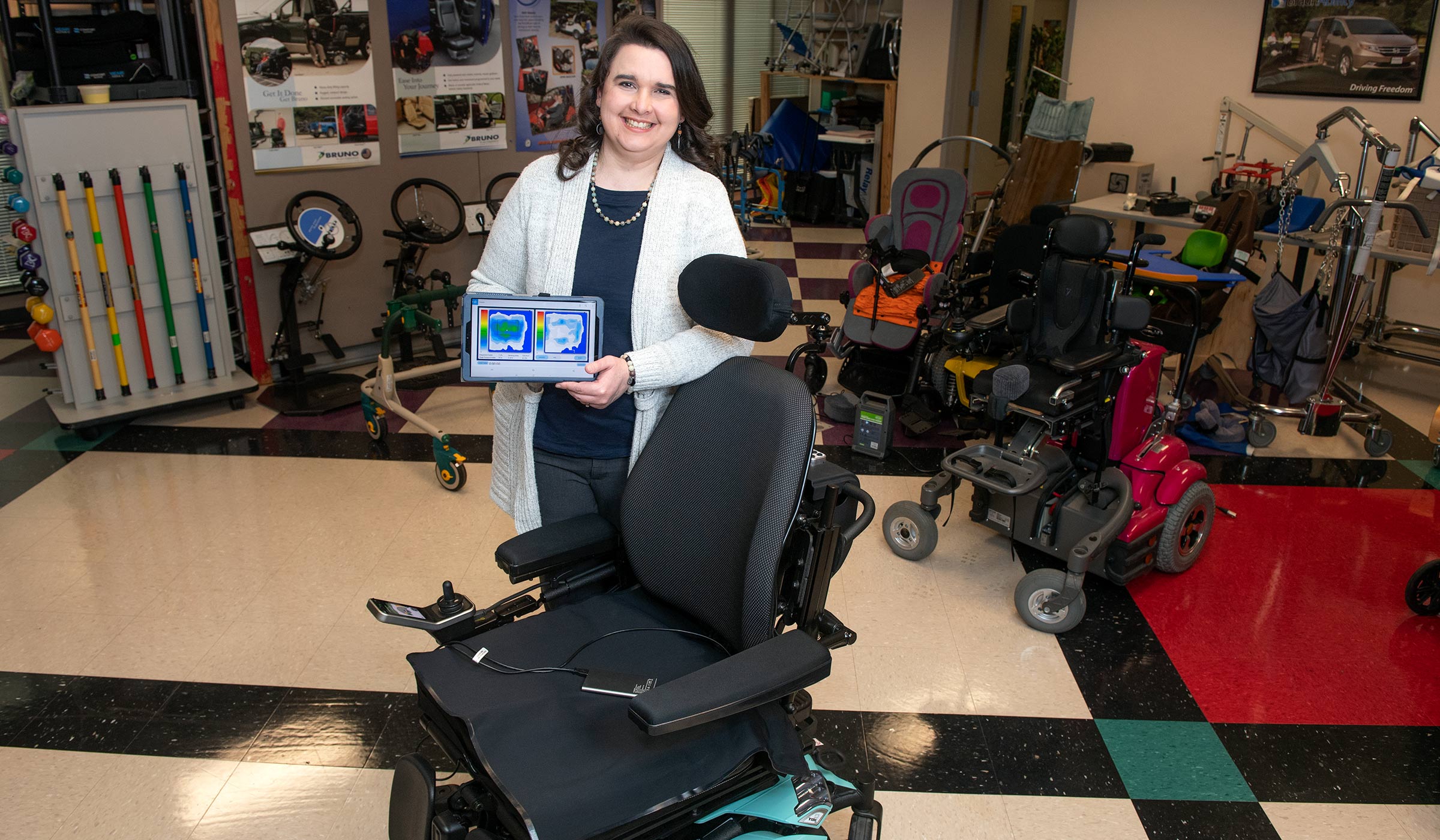 Rebecca Mathis standing in front of a wheelchair holding an iPad.
