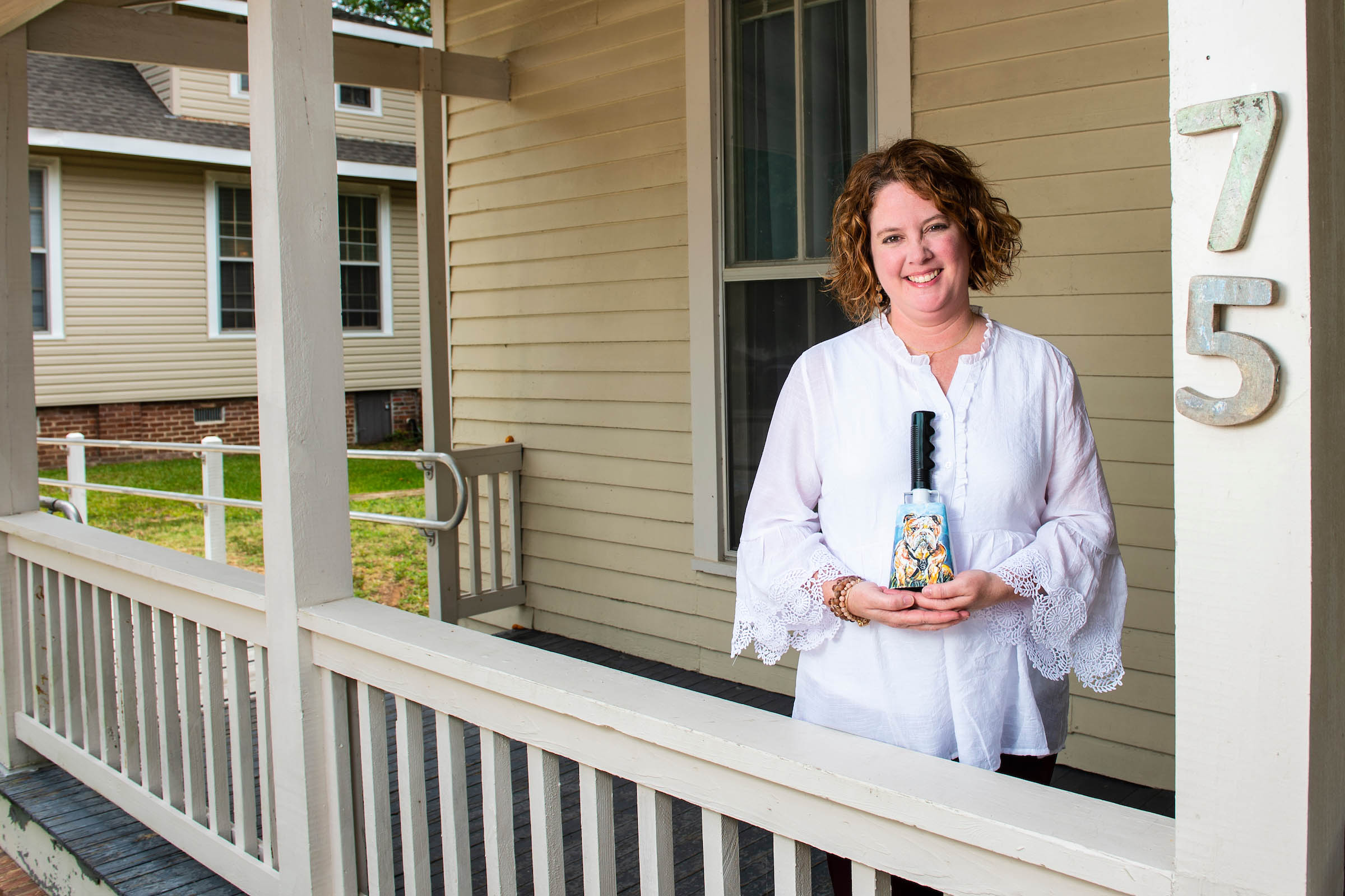 A photo of Christa King standing on a porch with a cowbell in her hand.