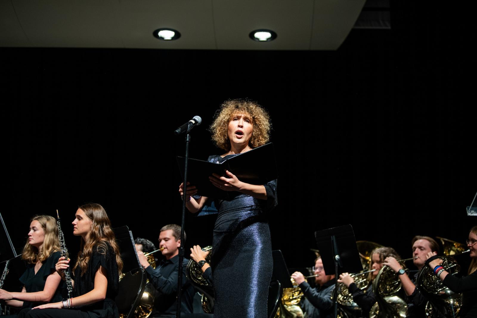Lady sings at mic with orchestra behind her