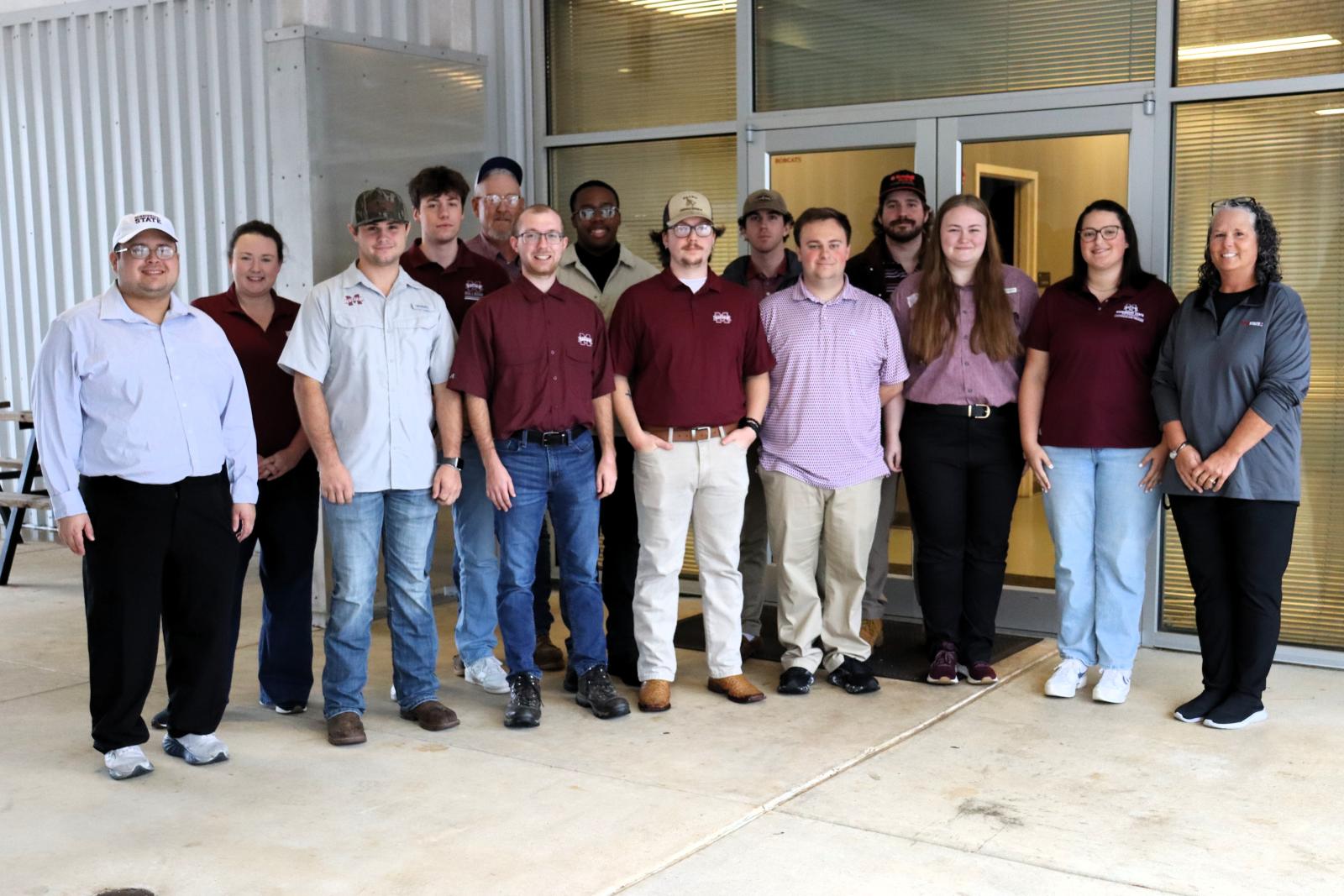A group of students and faculty pose for a photo outside a building