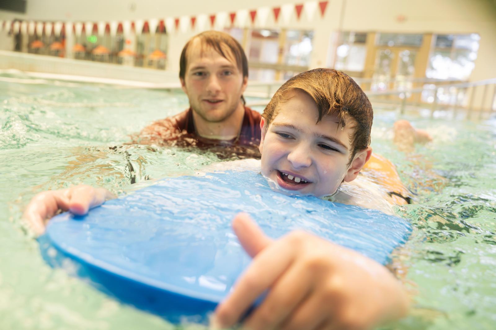 MSU swim instructor with child holding onto kickboard in a pool