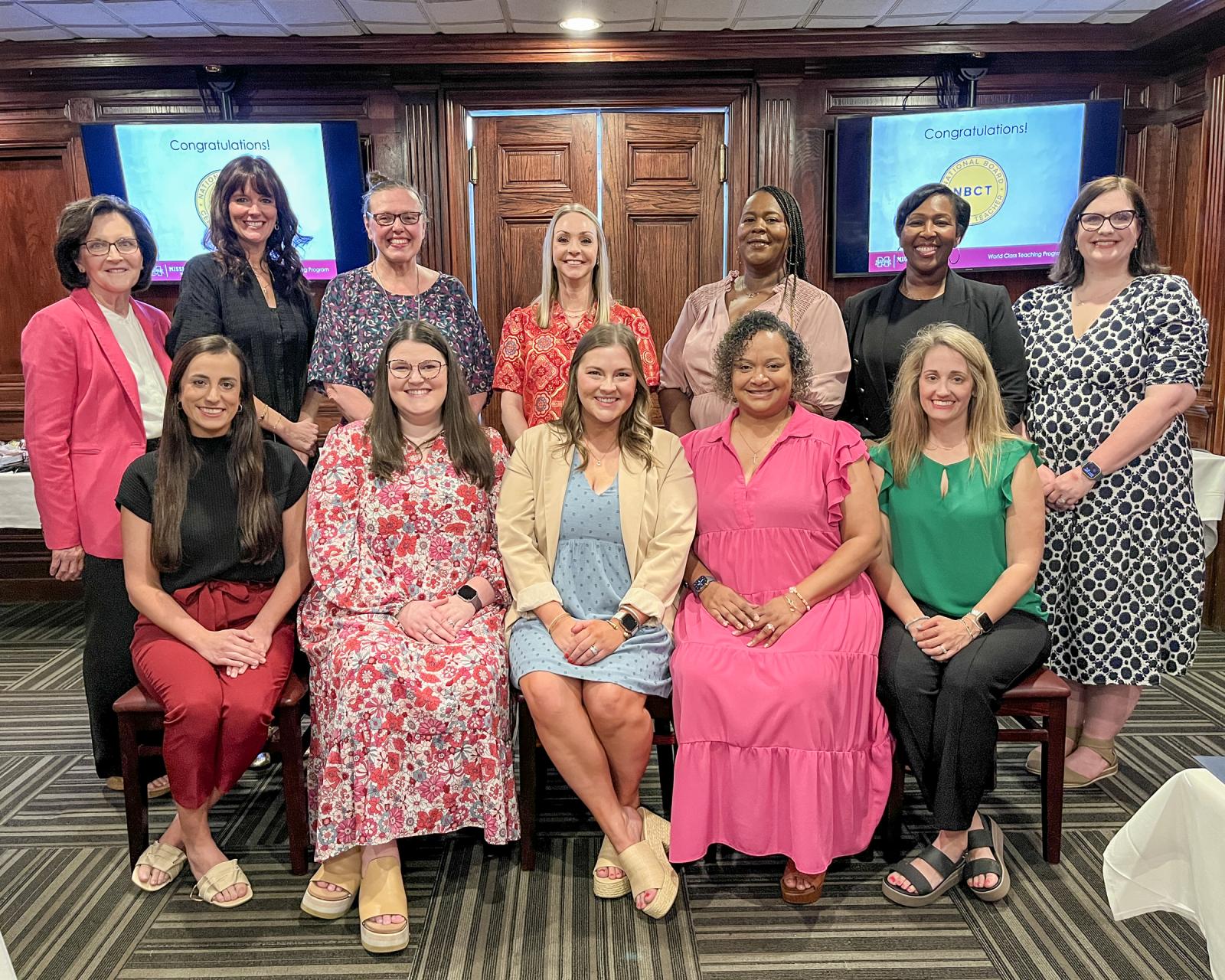 12 people pose for a photo, with five seated and seven standing behind them.