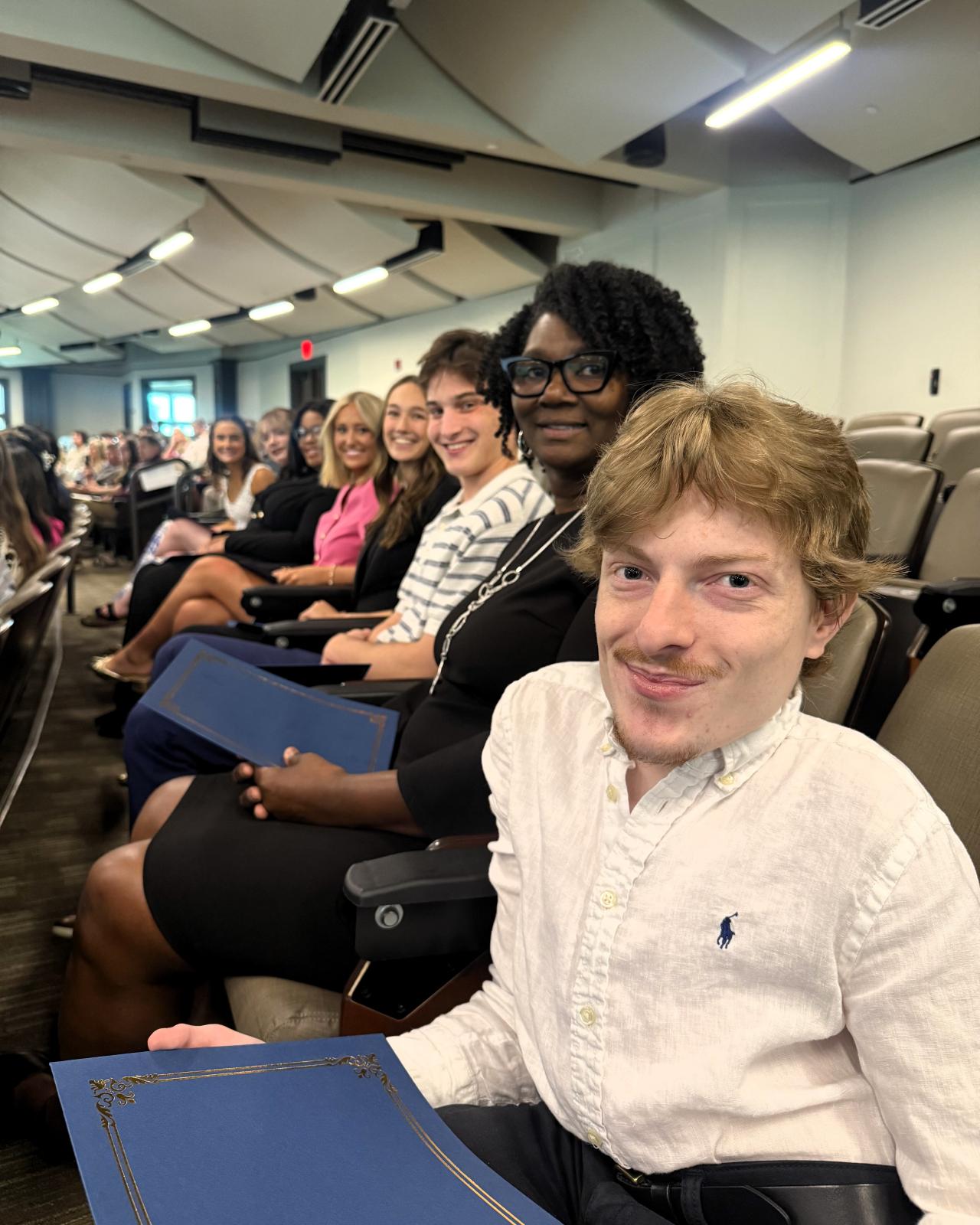 Eight students smile as they sit in the auditorium