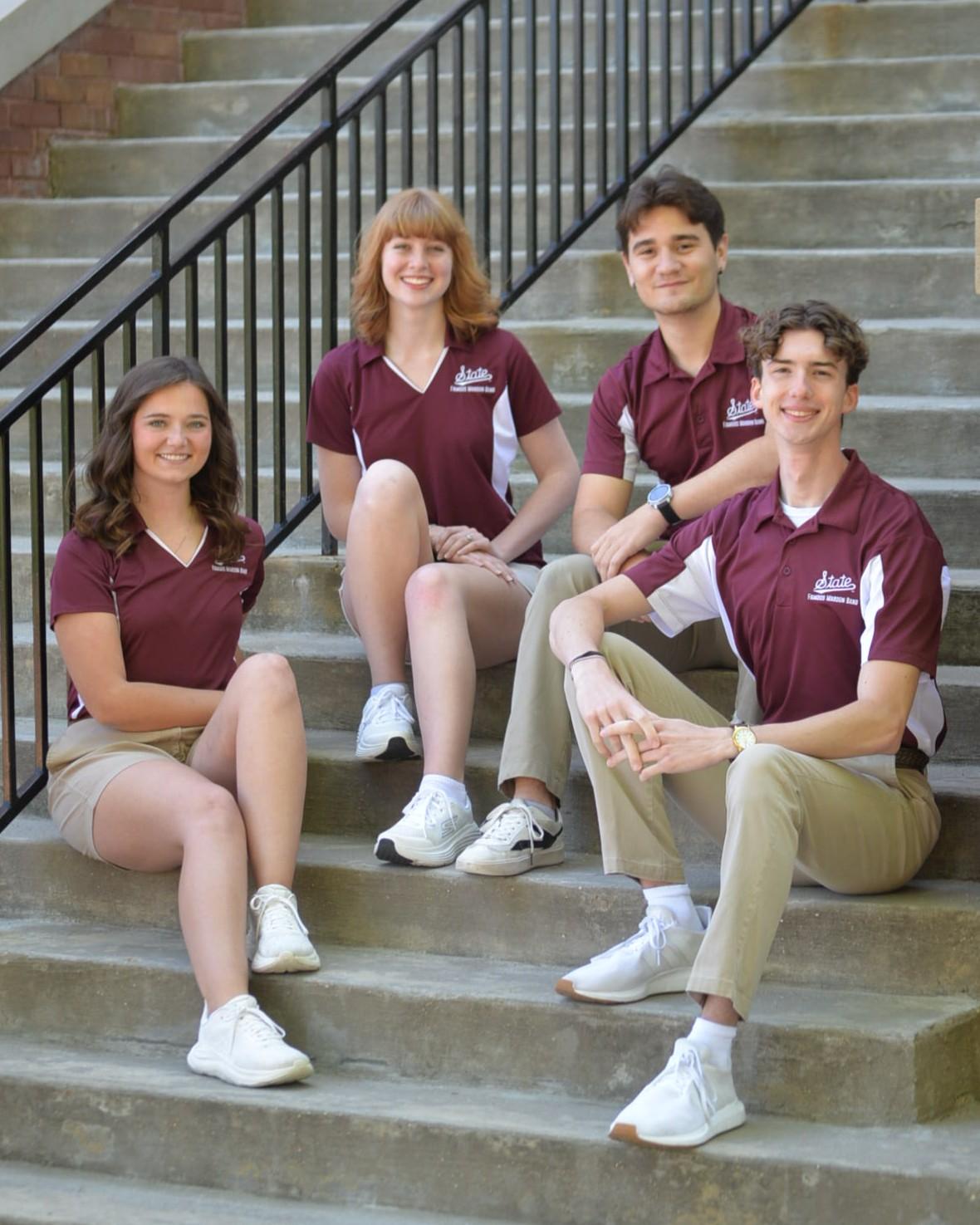 Photo of four students wearing maroon shirts, sitting on steps