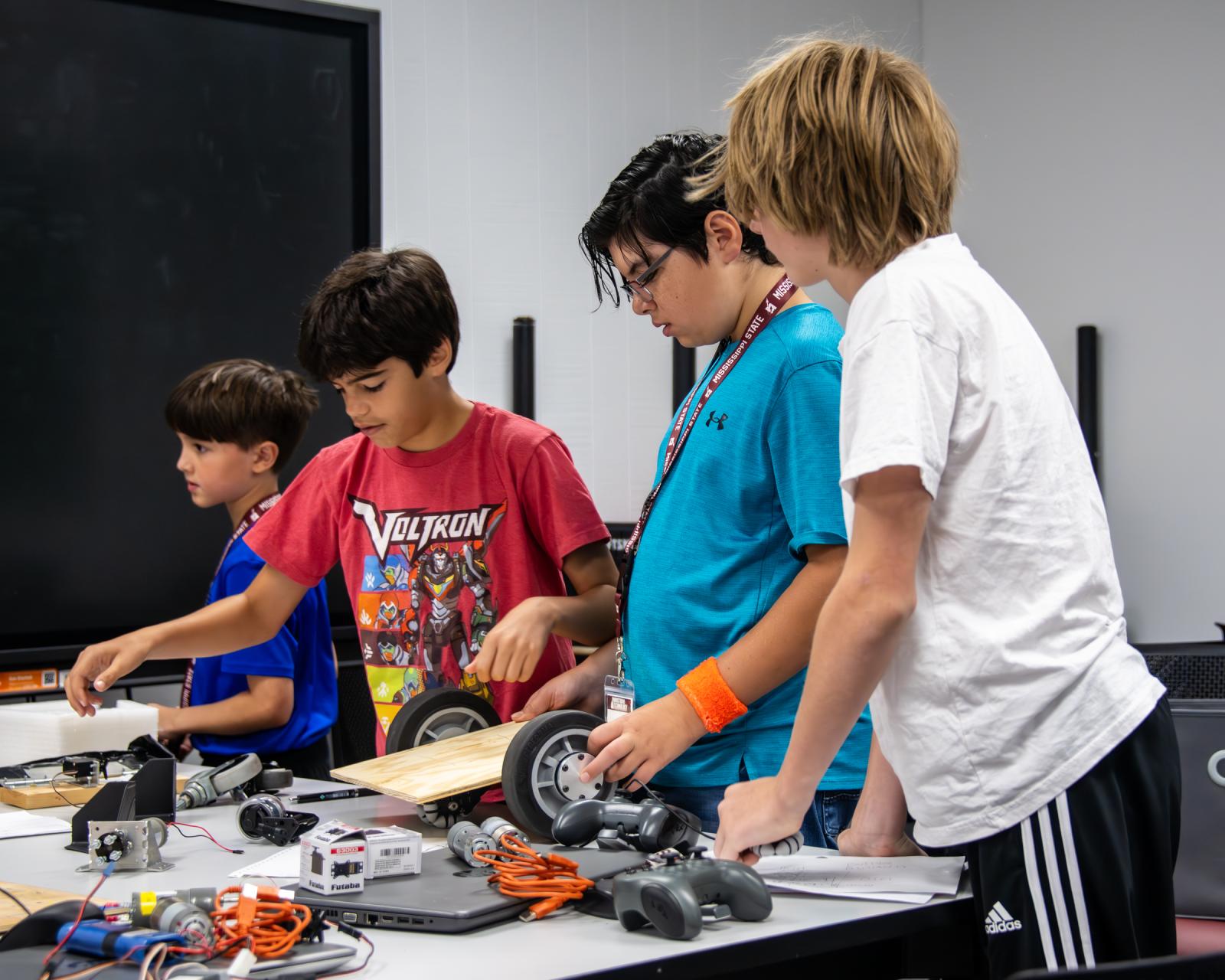 Four young boys build a robot together on a table