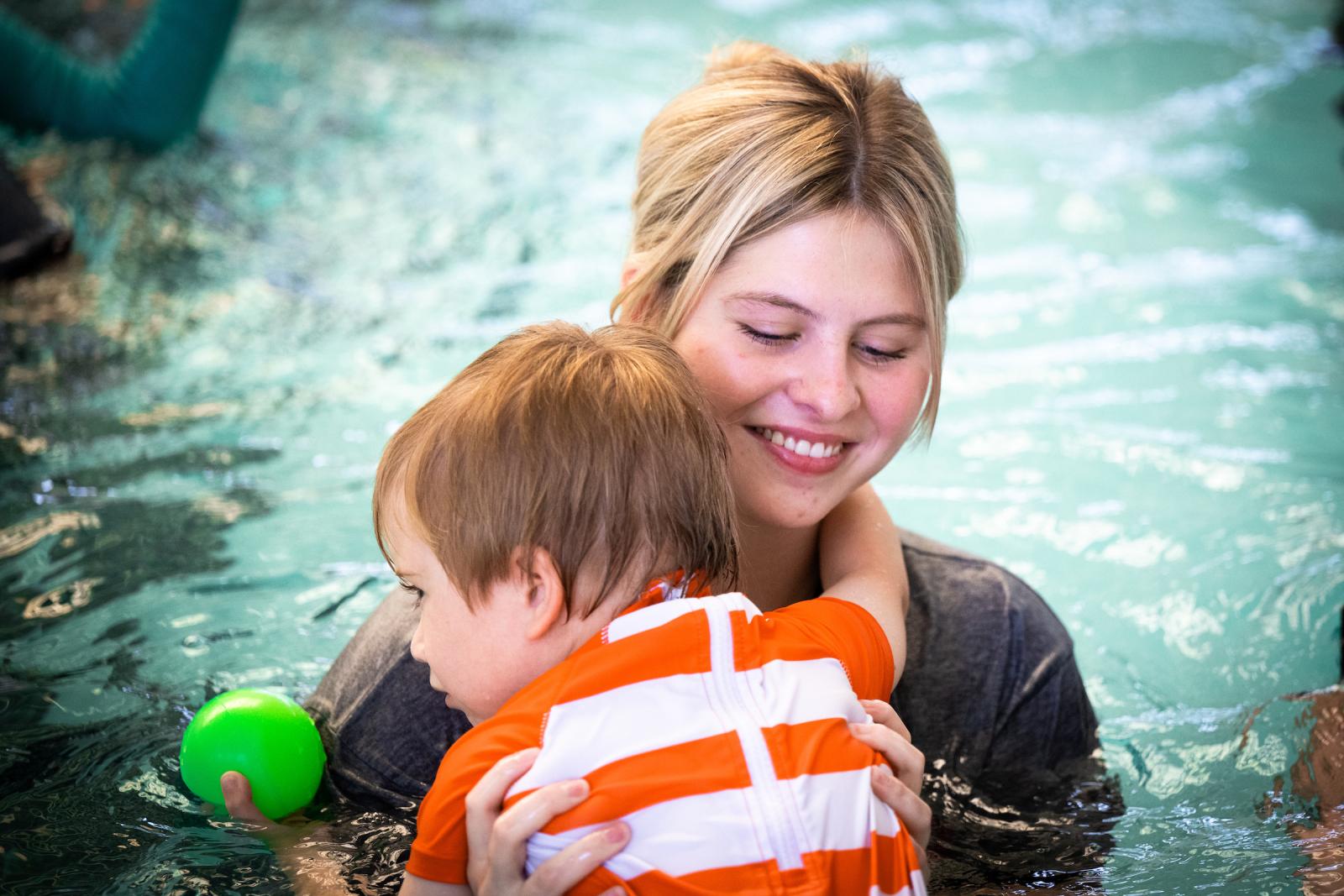 Adapted Swim Camp worker holds a child in the water