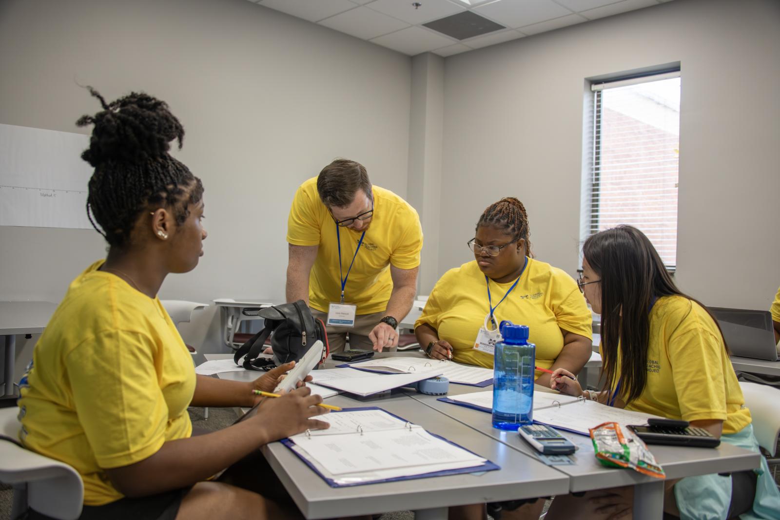 An instructor works with four students at a table in a classroom