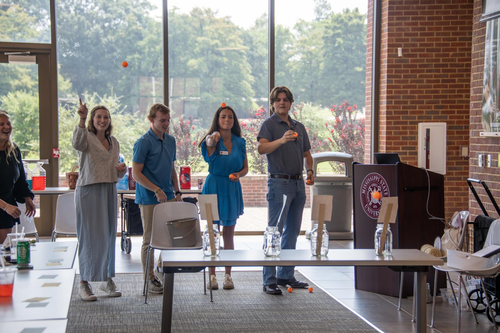 4 METP students throw small balls into a bottle as part of an exercise during a presentation on mental health