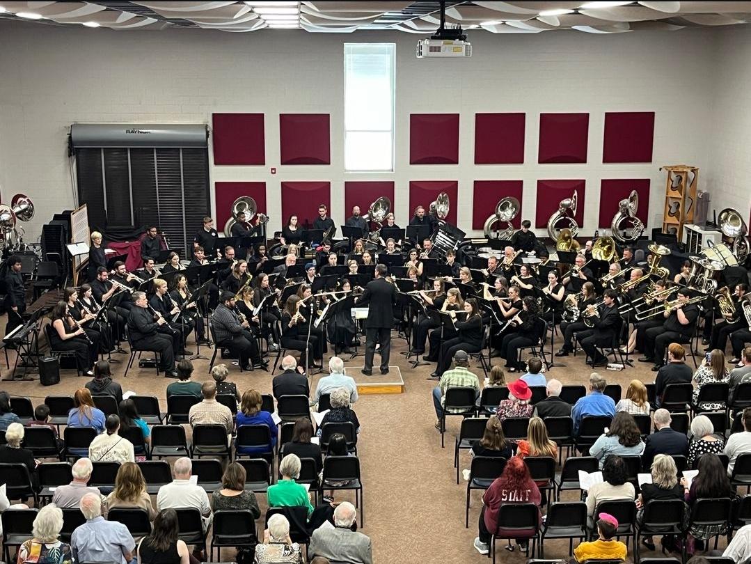 Community band performs in front of a large crowd inside a band hall