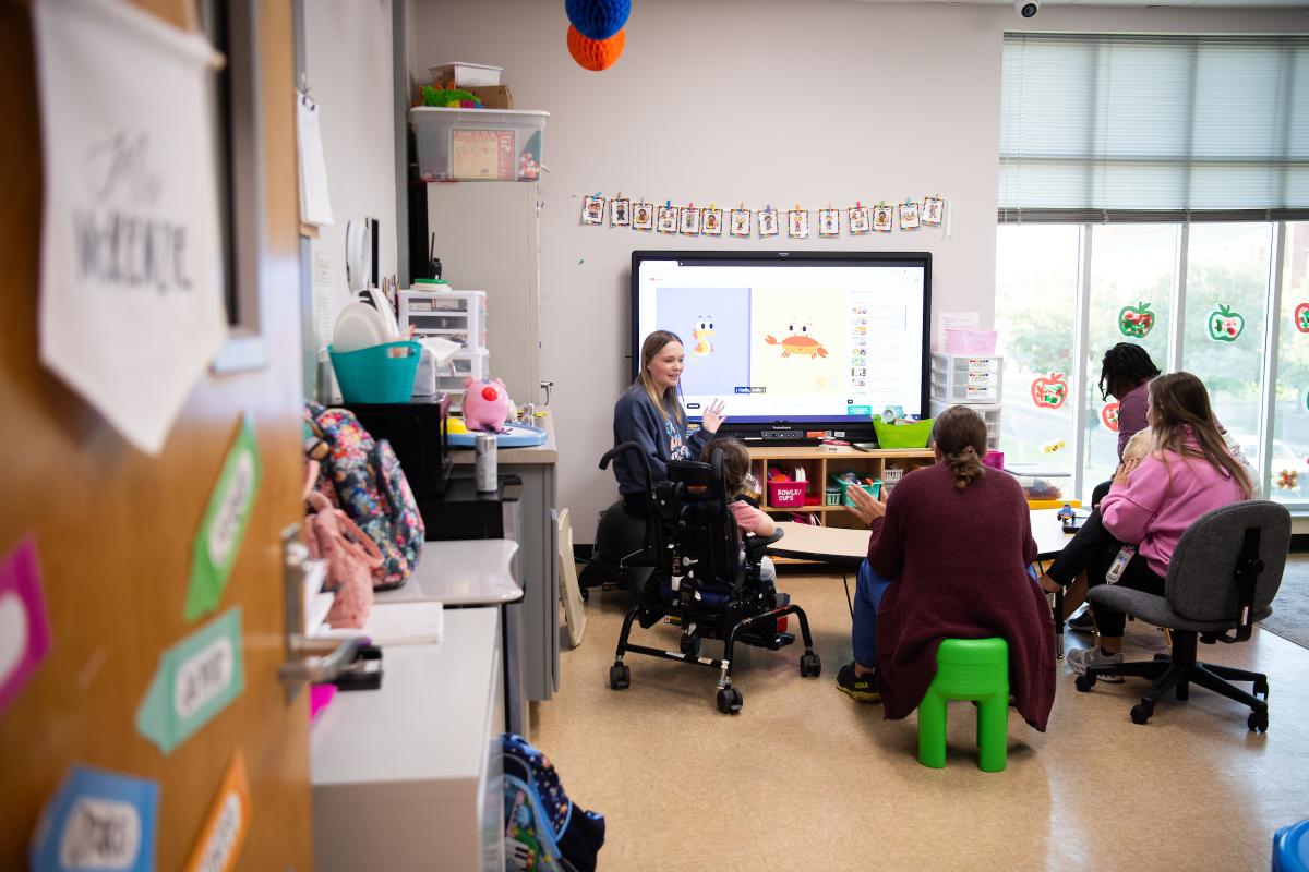 Classroom with teacher and students sitting around a table in front of a monitor
