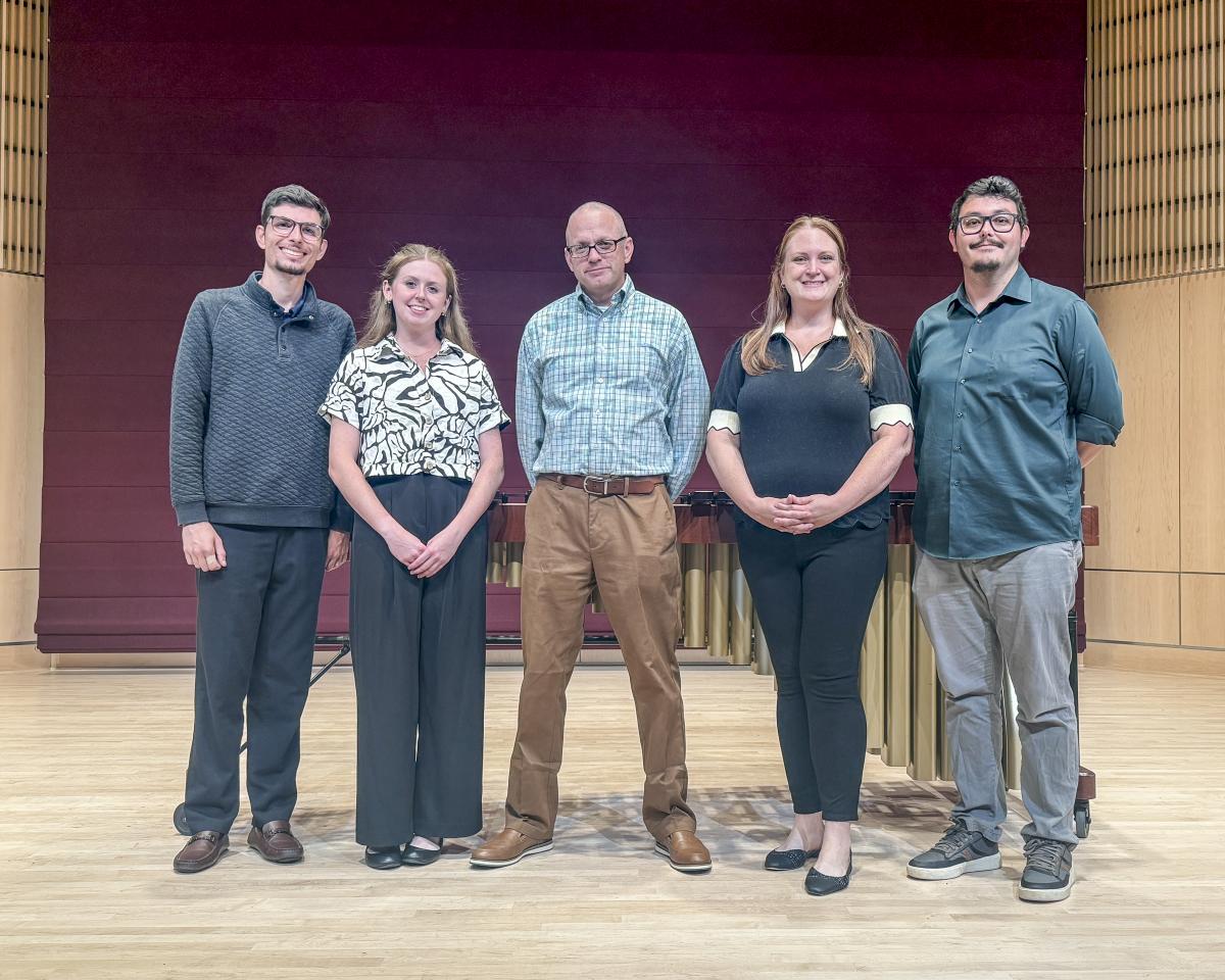 Five faculty and students pose for a photo onstage