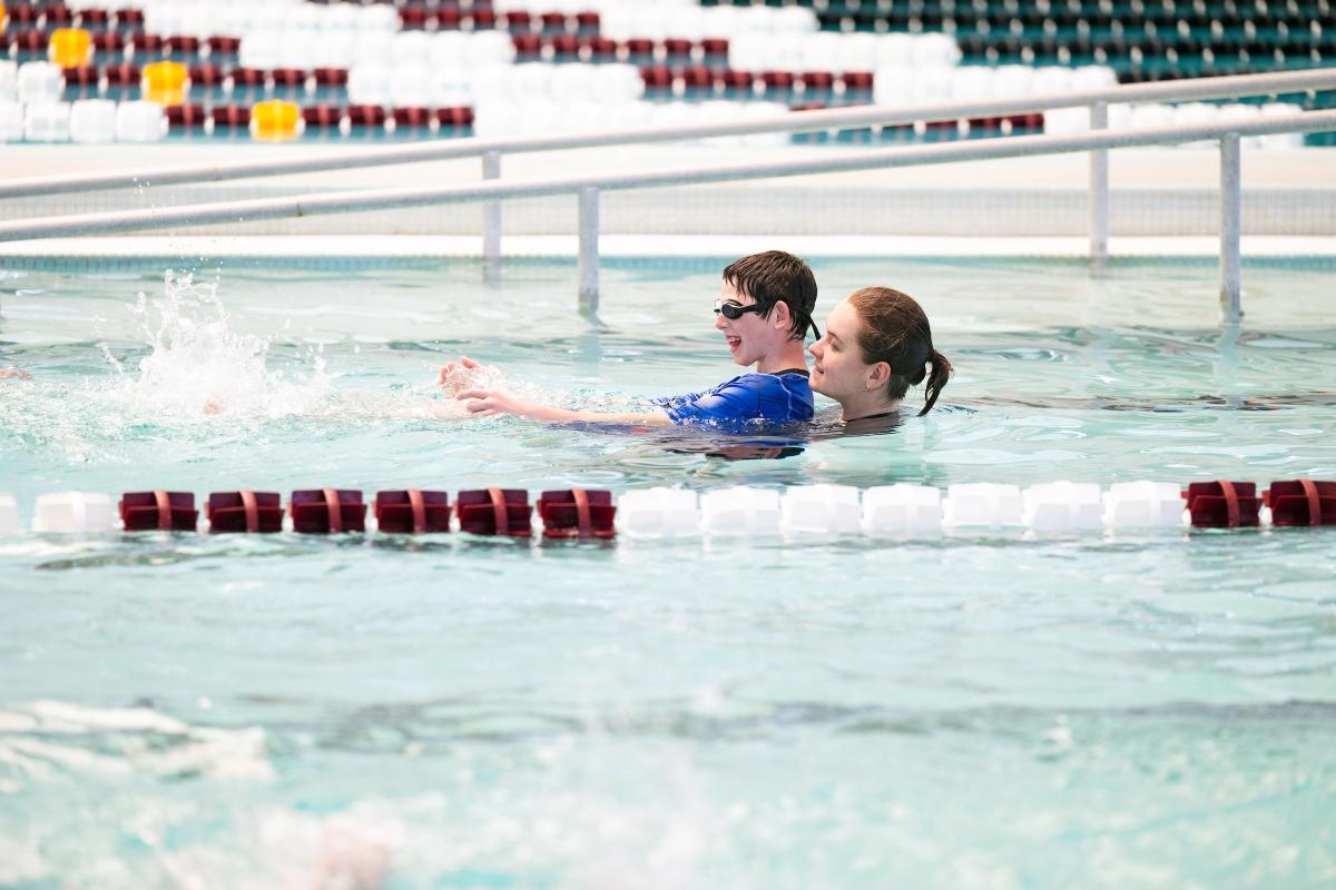 Instructor helps a child learn to swim in a pool.