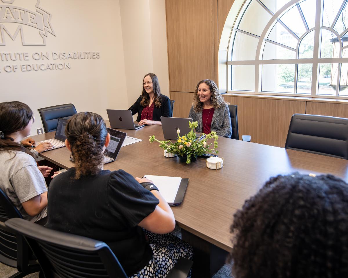 Two instructors sit a conference table with students
