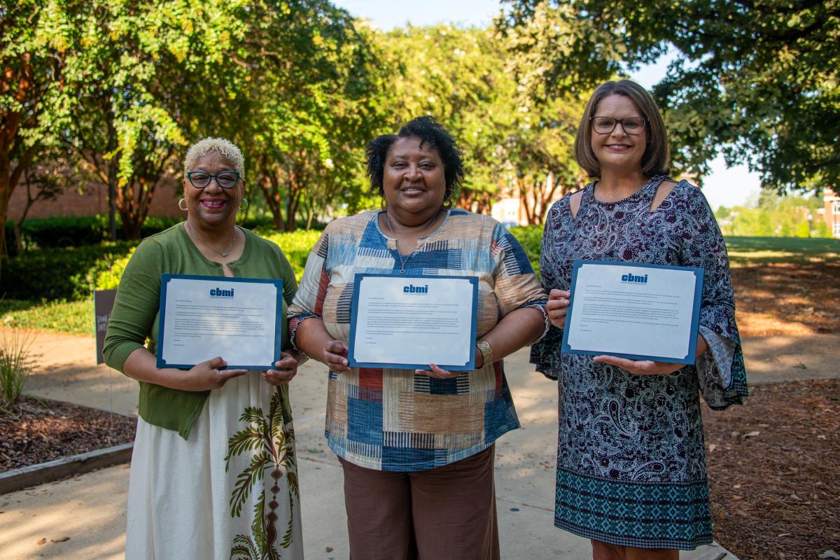 Three staff members hold certificates outside.