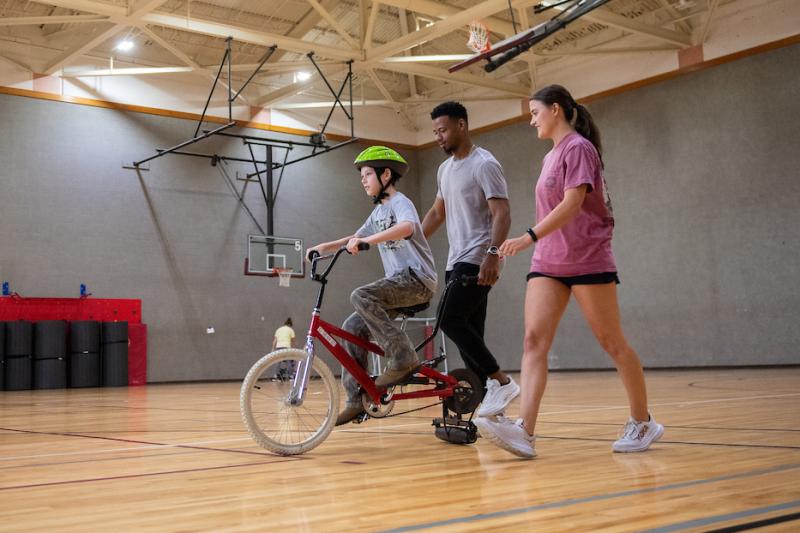 Young student on bike with two coaches in a gym
