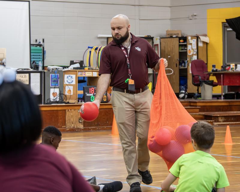 Physical education teaching handing ball to student in a gym